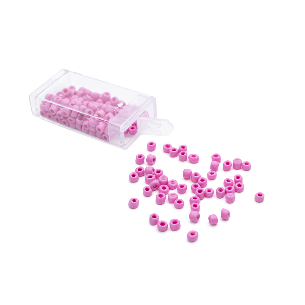 Aus einer kleinen, durchsichtigen Schachtel von Alexandra Renke ergießen sich rosa Rocailles-Perlen auf eine weiße Fläche und verleihen Ihren Kreationen mit diesen bezaubernden Glasperlen einen zarten Vintage-Touch.