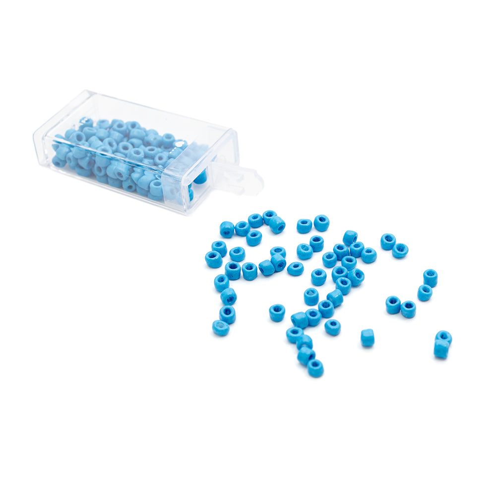 Kleine blaue Rocailles-Perlen von Alexandra Renke ergossen sich aus einem durchsichtigen Plastikbehälter auf eine weiße Fläche und verliehen ihr den Charme einer Vintage-Optik.