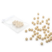 Alexandra Renke kleine, runde, cremefarbene Holzperlen - einige verpackt in einer durchsichtigen Plastiktüte, andere verstreut auf einer weißen Fläche.