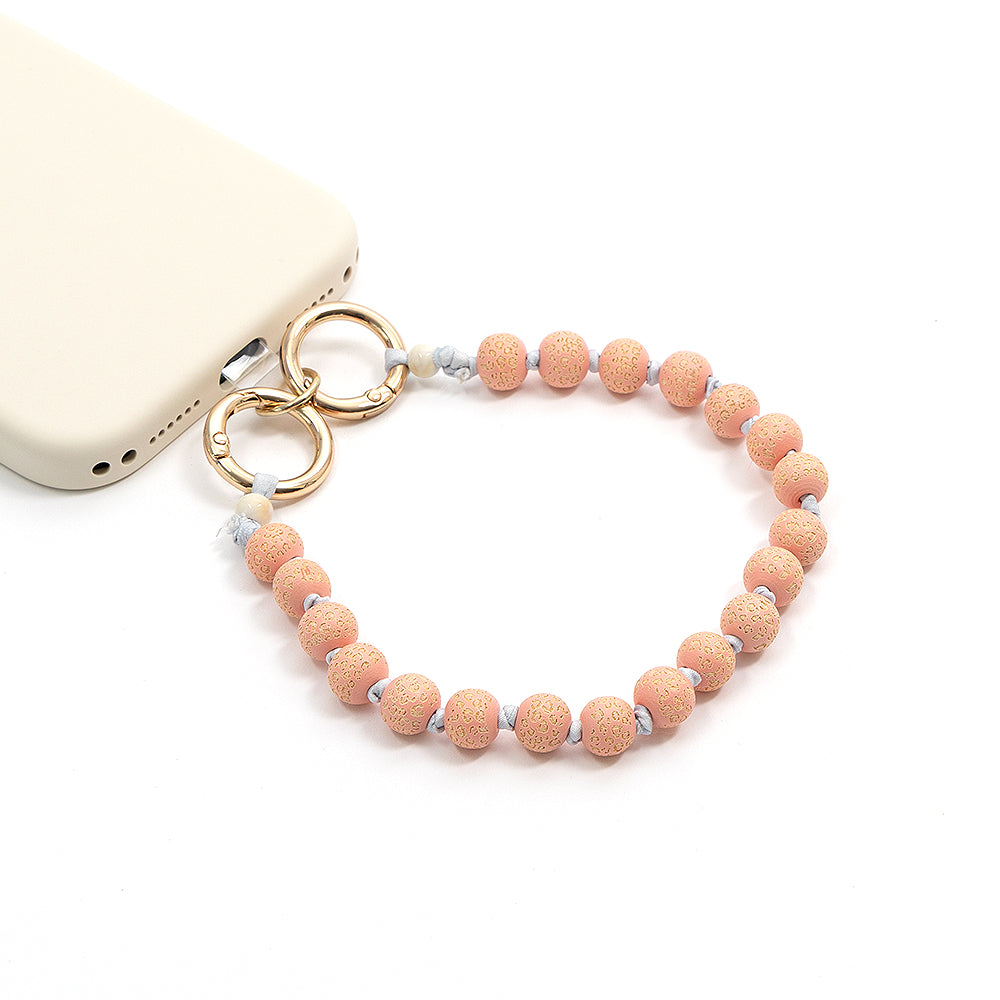 Eine beigefarbene Handyhülle von Alexandra Renke mit einem handgefertigten Perlenband aus rosa und weißen Holzperlen, das mit goldenen Ringen befestigt ist.