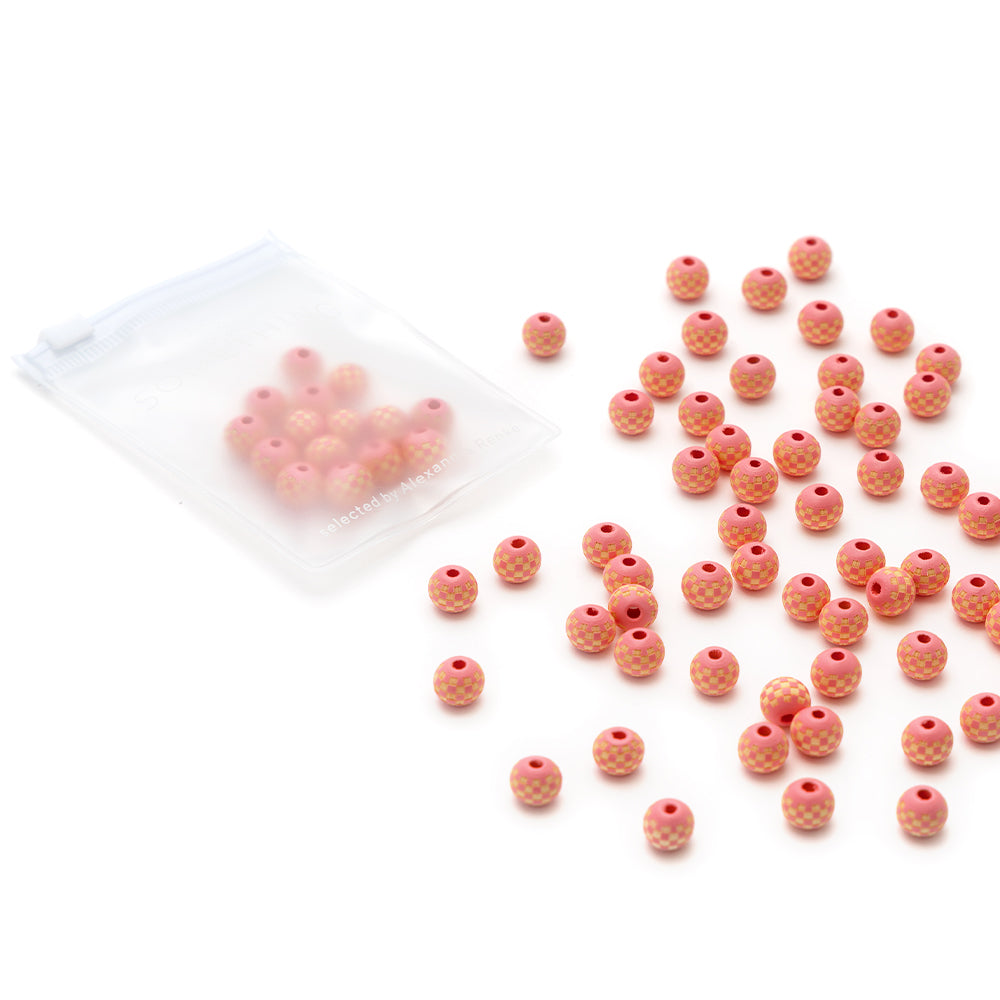Alexandra Renke kleine runde pfirsichrosa Holzperlen, einige verstreut und andere in einer Plastiktüte mit Reißverschluss, ausgestellt auf einem weißen Hintergrund.