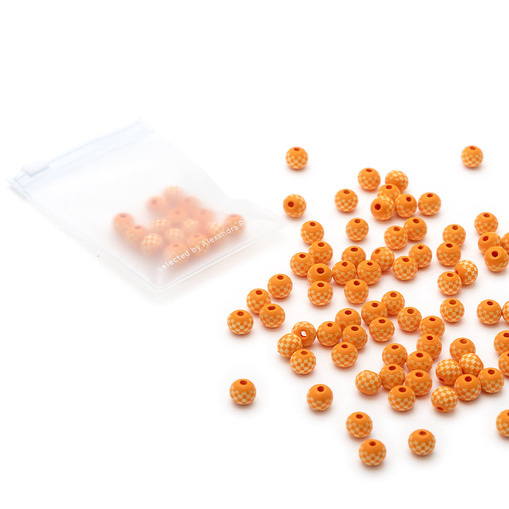 Kleine orangefarbene, strukturierte Perlen, möglicherweise handgefertigt, von Alexandra Renke liegen verstreut neben einem durchsichtigen Ziplock-Beutel mit weiteren identischen Perlen.