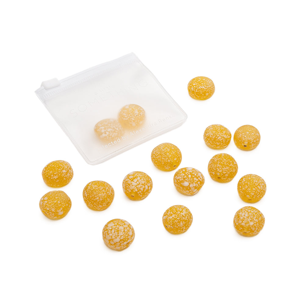 Vierzehn gelbe Bonbons mit einer rissigen Oberfläche, die an matte Glasperlen erinnern, quellen aus einem durchsichtigen Reißverschlussbeutel vor einem weißen Hintergrund hervor. Mit Produktdaten überarbeitet: Vierzehn gelbe Bonbons von Alexandra Renke mit einer rissigen Oberfläche, die an matte Glasperlen erinnert, quellen aus einem durchsichtigen Reißverschlussbeutel vor einem weißen Hintergrund hervor.