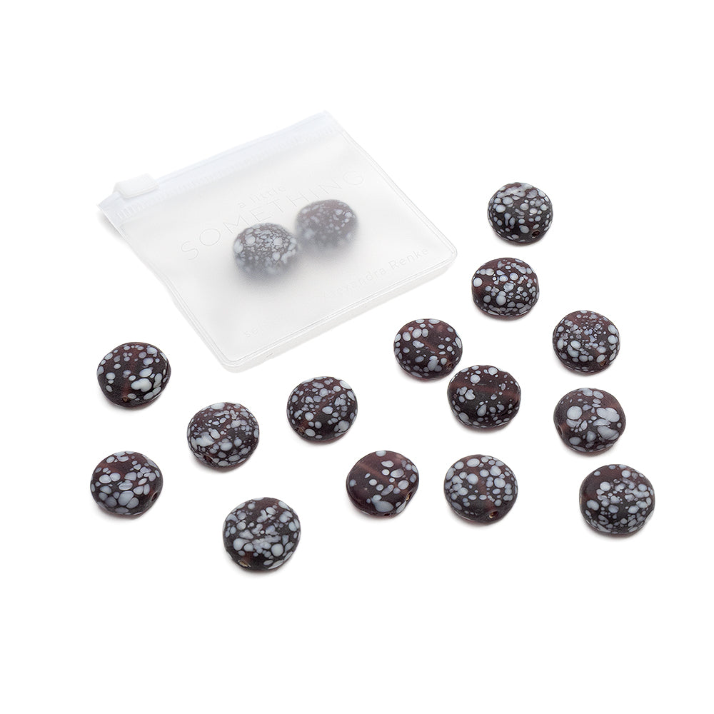 Vierzehn matte, glasperlenähnliche dunkle Bonbons mit weißen Sprenkeln, von denen einige in einem mattierten, wiederverschließbaren Beutel von Alexandra Renke verpackt sind. Ideal für kreative Bastelprojekte oder als einzigartige dekorative Note.