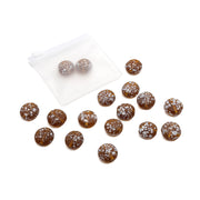 Ein kleiner Beutel von Alexandra Renke mit braunen, runden Bonbons, die mit weißen Sprenkeln überzogen sind, ist auf einer weißen Fläche ausgebreitet und erinnert an runde Glasperlen – perfekt für kreative DIY-Projekte.