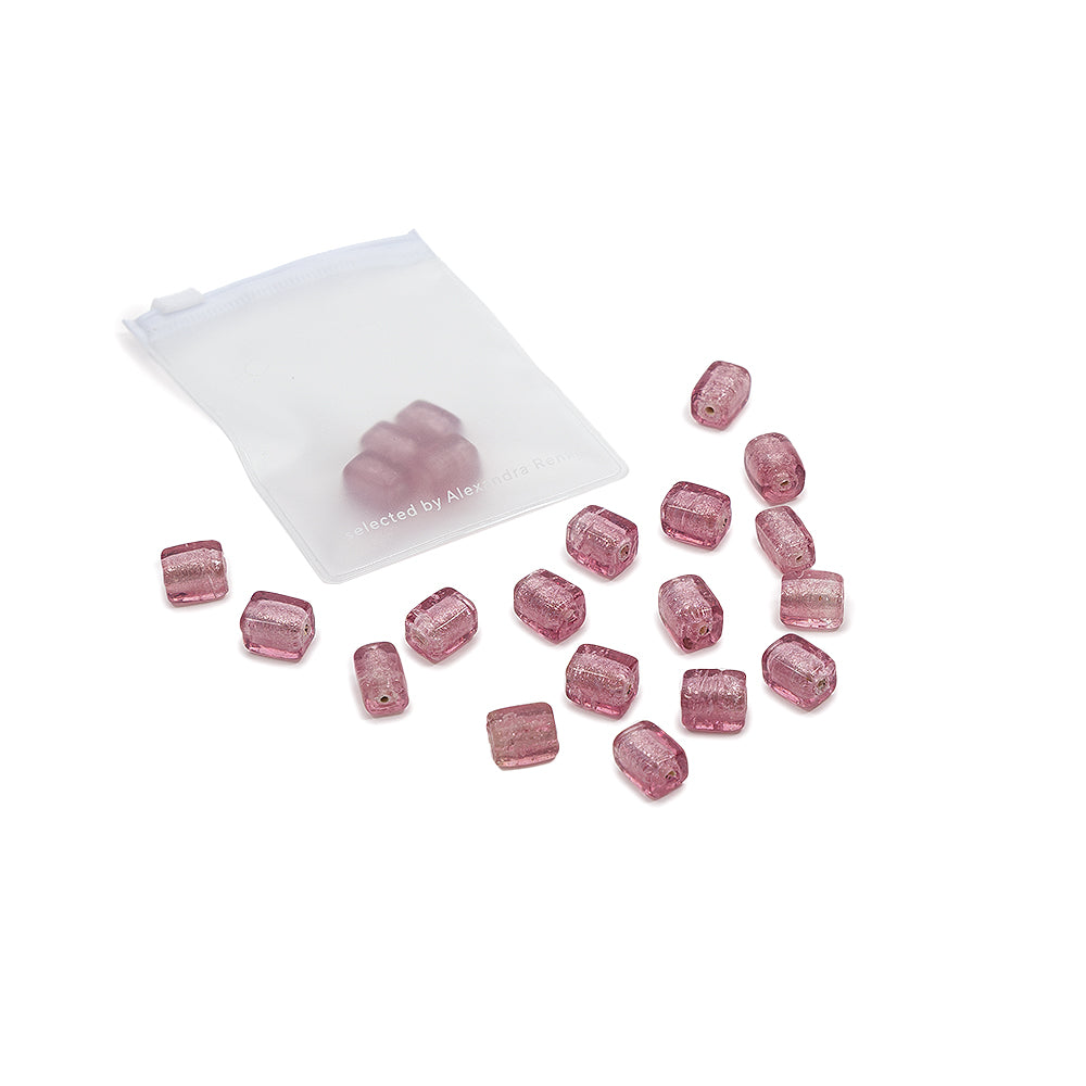 Kleine, matt-rosa Glasperlen rieseln aus einem halbtransparenten weißen Beutel auf eine weiße Fläche – ideal für DIY-Projekte und kreative Gestaltungen.