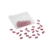 Durchsichtiger Beutel mit rosa, kapselartigen Tabletten, die auf weißem Hintergrund verstreut sind – die perfekte Inspiration für DIY-Projekte oder um Handarbeitskreationen einen Farbtupfer zu verleihen.