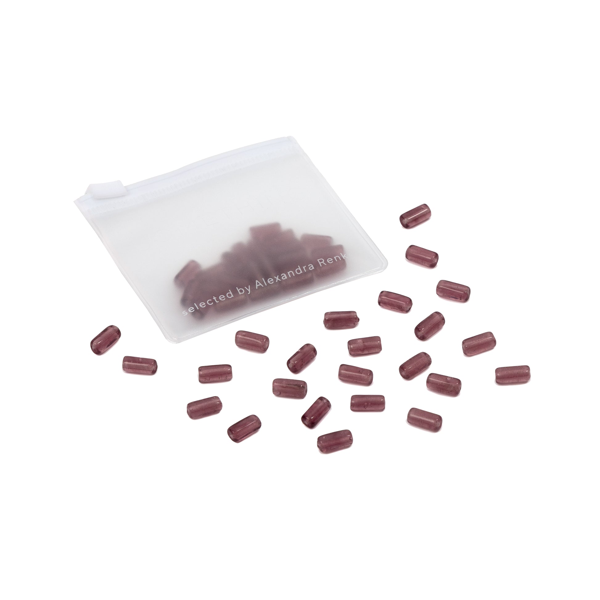 Ein weißer Beutel mit vereinzelten braunen, kapselförmigen Tabletten und handgefertigten Glasperlen auf weißem Hintergrund.