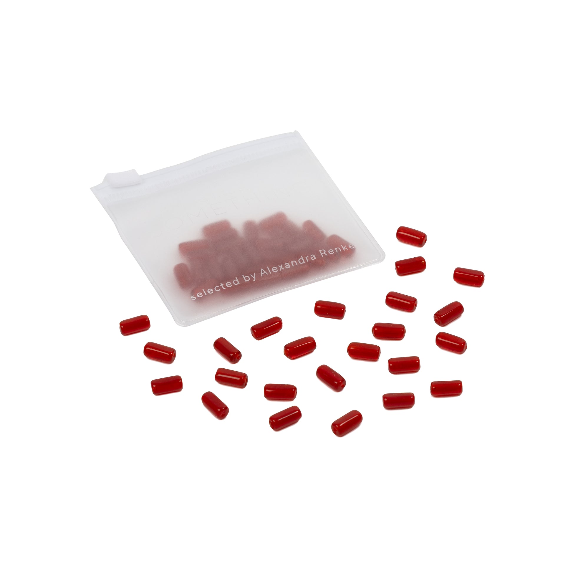 Kleine rote Kapseln, die an Glasperlen erinnern, quellen aus einem durchsichtigen Beutel mit Reißverschluss auf weißem Hintergrund hervor – ein perfekter Fund für Handarbeiten oder kreative DIY-Projekte.