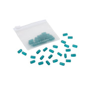 Kleine blaugrüne Kapseln, verstreut vor einem durchscheinenden weißen Beutel mit Reißverschluss, in dem sich weitere Kapseln befinden – ideal für Handarbeit und DIY-Projekte oder in Kombination mit Glasperlen für kreative Projekte.