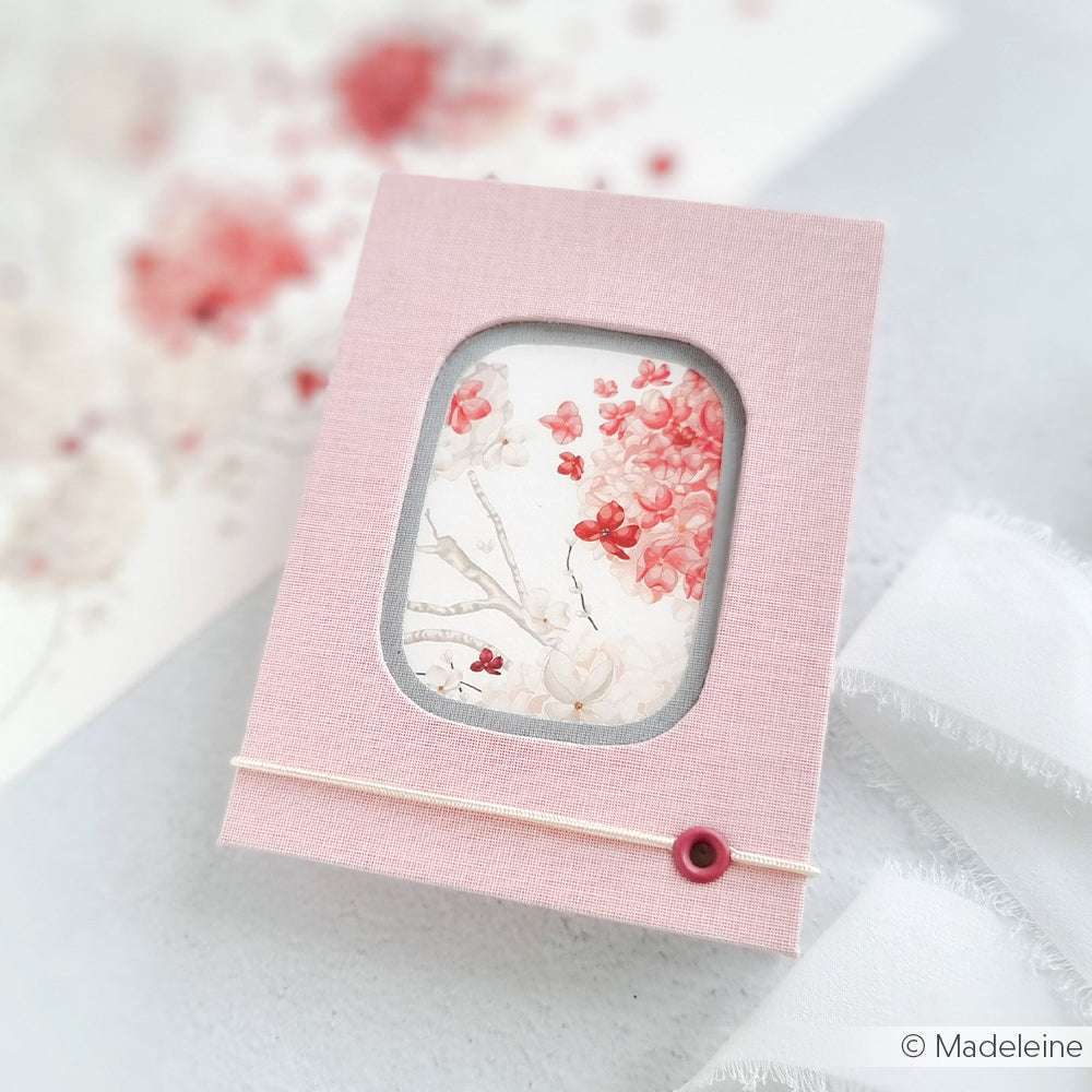 Ein rosa strukturiertes Buchbinden-Notizbuch von Alexandra Renke mit einem Fenster, das ein florales Kunstwerk zeigt, mit einer Schnur gebunden und mit einem rosa Knopf versehen.