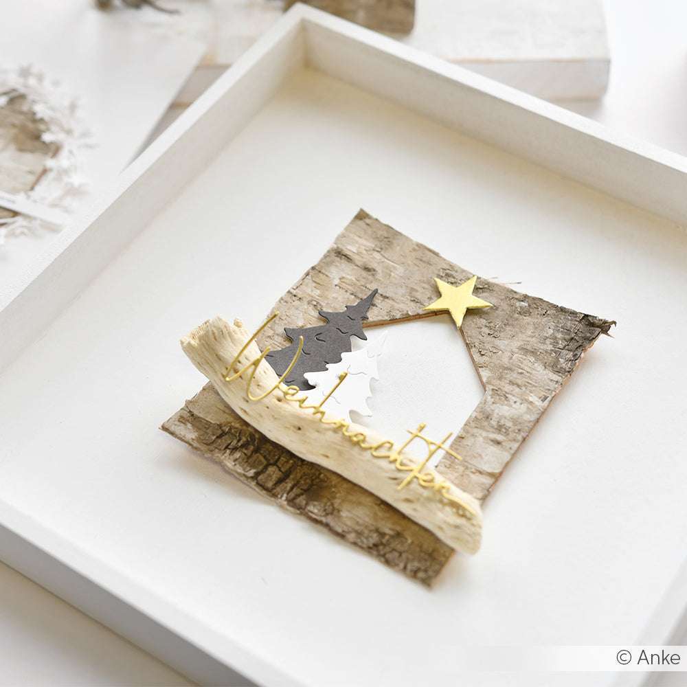 Eine rustikale Weihnachtsszene mit Bäumen und einem Stern, gefertigt aus Birkenrinde und Holz in einem weißen Rahmen - ein charmantes Werk von Alexandra Renke.