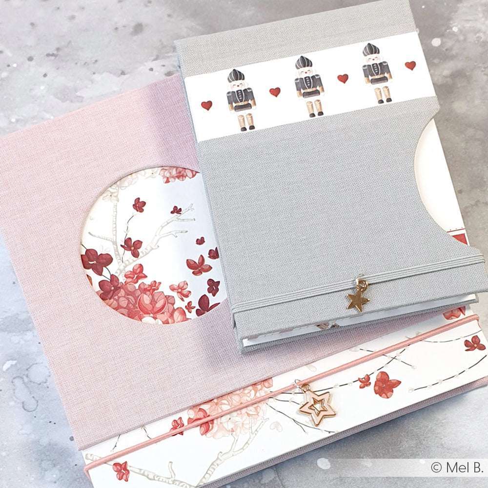 Zwei dekorative Alexandra Renke-Notizbücher mit Blumen- und Nussknackermotiven und sternförmigen Bandanhängern - ideal für Buchbinden-Liebhaber und Fans von feinen Details.