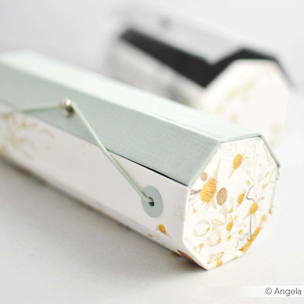 Achteckige, floral gemusterte Schachtel von Alexandra Renke mit hellgrünem Deckel und Schnurverschluss. Sie ist mit präzisen PAPPcut-Achteck-Winkeln gefertigt und zeigt fachmännische Buchbindetechniken - eine verschwommene Schachtel erscheint im Hintergrund.