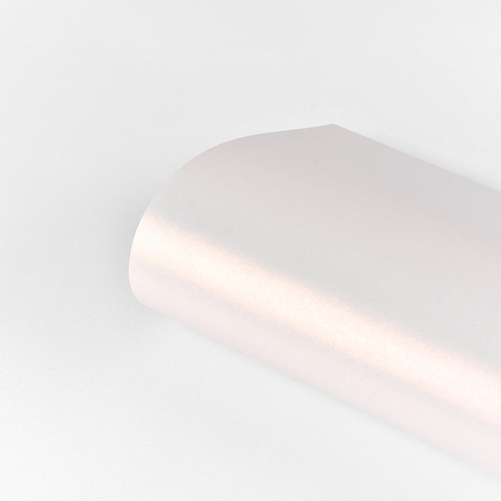 Ein gerollter Bogen ☆ Schimmer-Effekt Papier in Hellrosa, 310 g/m², ruht auf weißem Hintergrund und unterstreicht die elegante Papierkunst mit einem dezenten Schimmer.