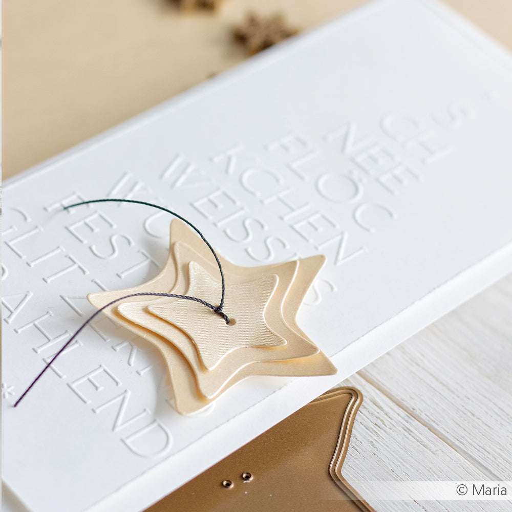 Grußkarte von ☆ aus 310 g/m² Schimmer-Papier, mit geprägtem weißem Text und gestapelten goldenen Stern-Ornamenten, die mit schwarzem Garn gebunden sind - ein raffiniertes Stück Papierkunst.