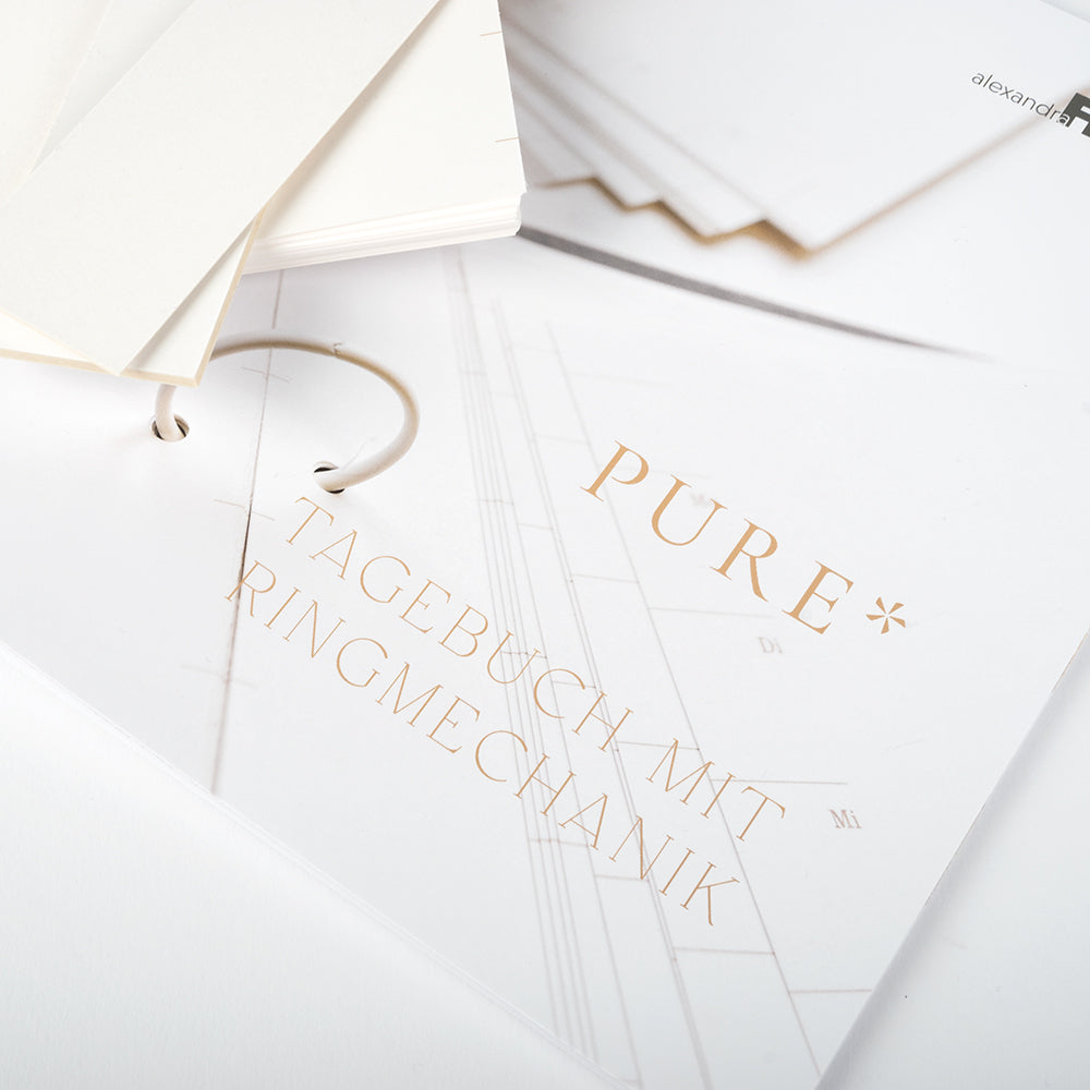Offener Ringbuchplaner von Alexandra Renke mit "PURE* TAGEBUCH MIT RINGMECHANIK" in Gold auf weißem Umschlag - perfekt für dein eigenes Tagebuch erstellen oder als Wochenplaner Materialkit.