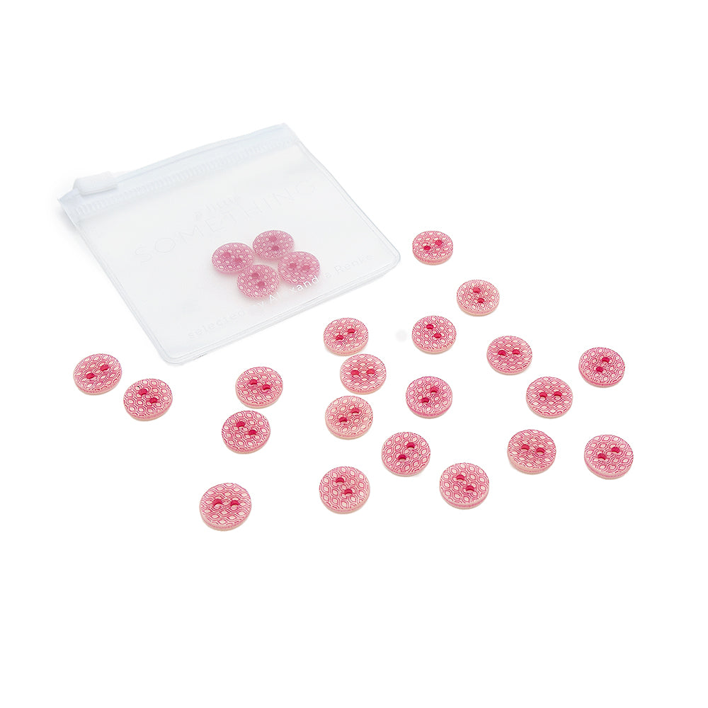 Zwanzig kleine, rosa gemusterte Knöpfe von Alexandra Renke mit weißen Sprenkeln, einige lose, andere in einem durchsichtigen Plastikbeutel.
