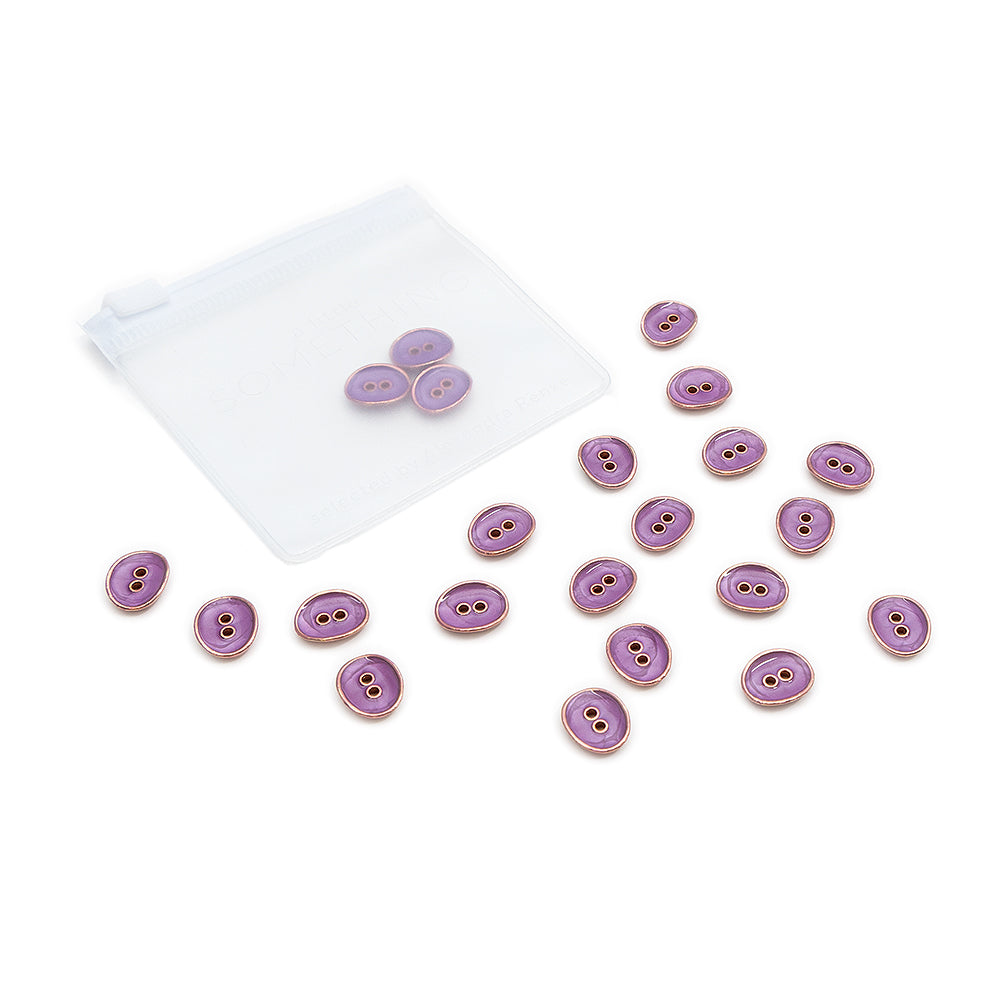 Ein kleines durchsichtiges Tütchen und mehrere edle ovale Knöpfe von Alexandra Renke in elegantem Violett, jeweils mit zwei Löchern, liegen verstreut auf einer weißen Fläche.