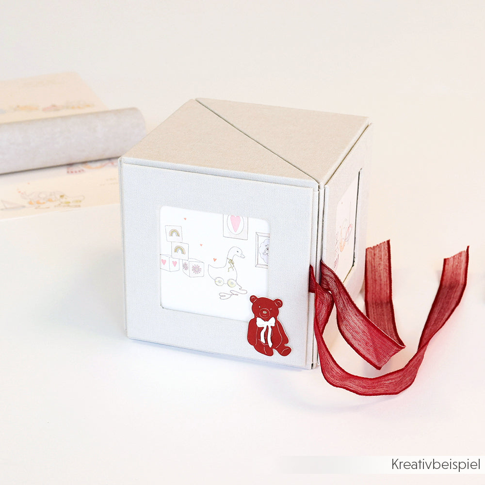 Die graue Fotowürfelbox von Alexandra Renke ist mit einer roten Schleife und einer Teddybär-Illustration verziert und verfügt über ein Fenster, das charmante Tierzeichnungen zeigt.