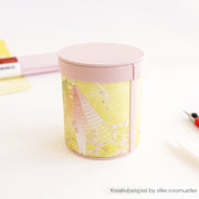 Runde, pastellrosa-gelbe Blechdose mit einem Blumenmuster von Alexandra Renke, ideal als PAPPKit-Geschenkbox, präsentiert auf einem weißen Untergrund.