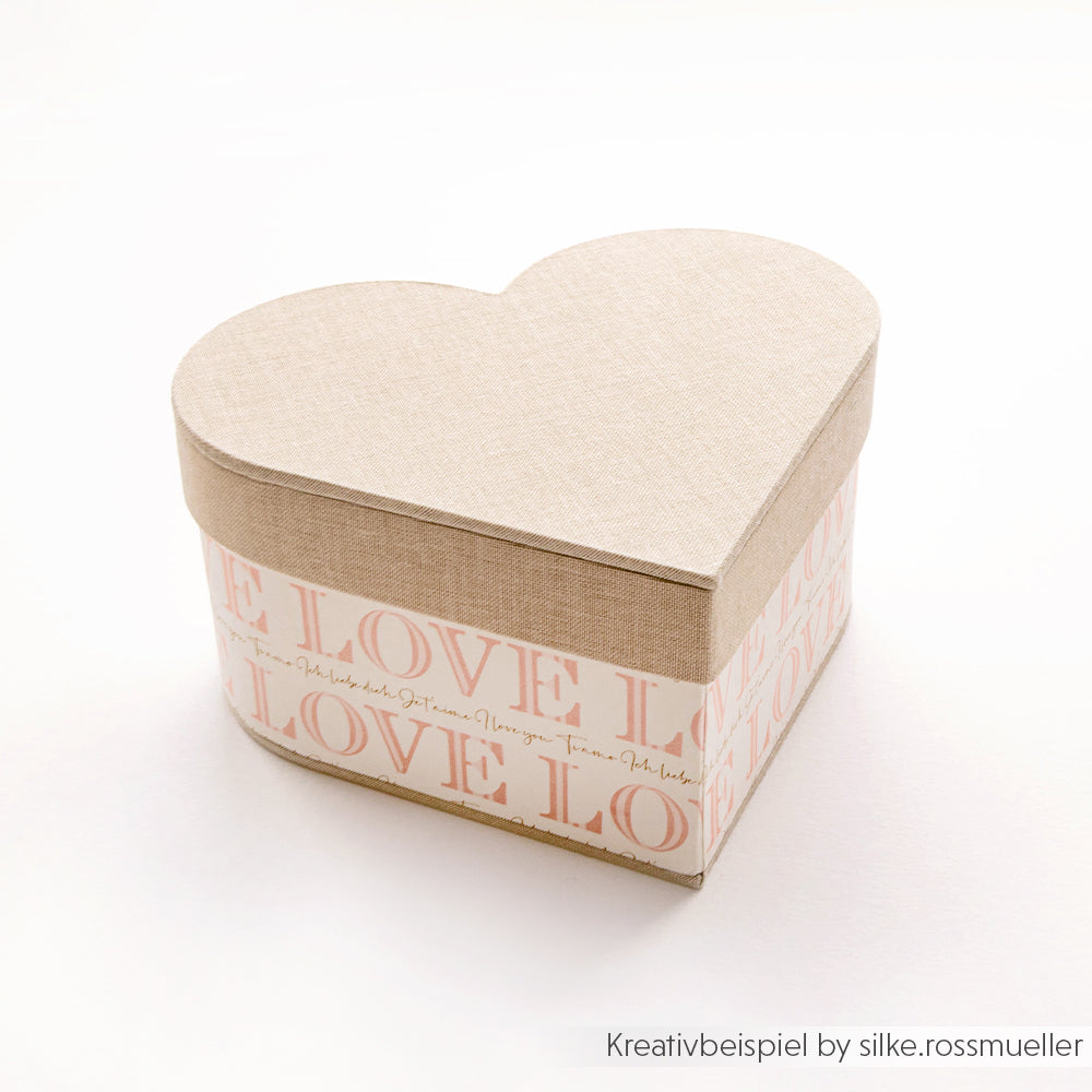 Beigefarbene DIY-Geschenkbox in Herzform von Alexandra Renke mit der Aufschrift „LOVE“ und einem Schriftzugmuster an den Seiten, abgebildet auf weißem Hintergrund.