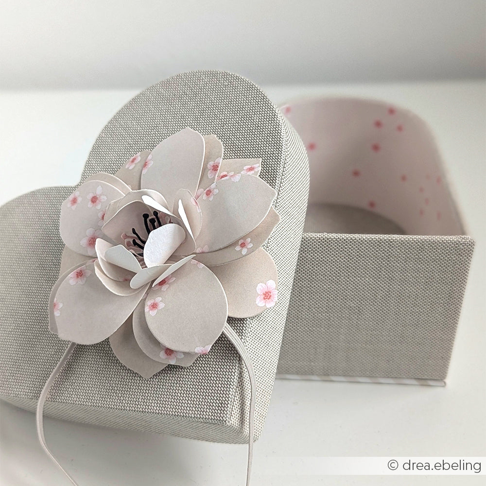 Alexandra Renke Herzbox als bezaubernde Geschenkverpackung, mit einer rosafarbenen Papierblume auf dem Deckel, leicht geöffnet auf weißer Fläche - ideal für Herzbox basteln Projekte und kreative Geschenkideen.
