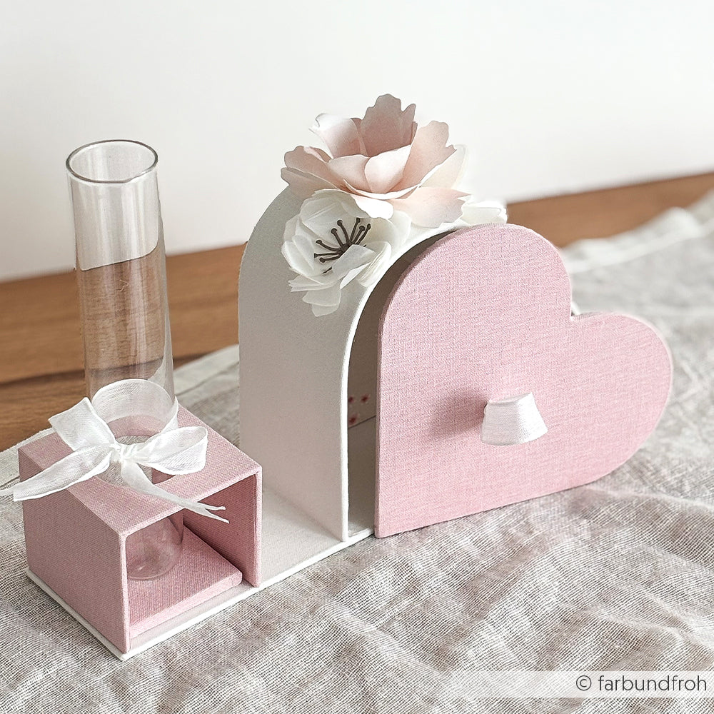 Die rosa-weiße Geschenkbox in Herzform mit Papierblumen und einer Glasvase mit Schleifenband auf Leinen von Alexandra Renke ist ideal, um Ihr PAPPKit zu verschönern oder Herzbox basteln zu inspirieren.