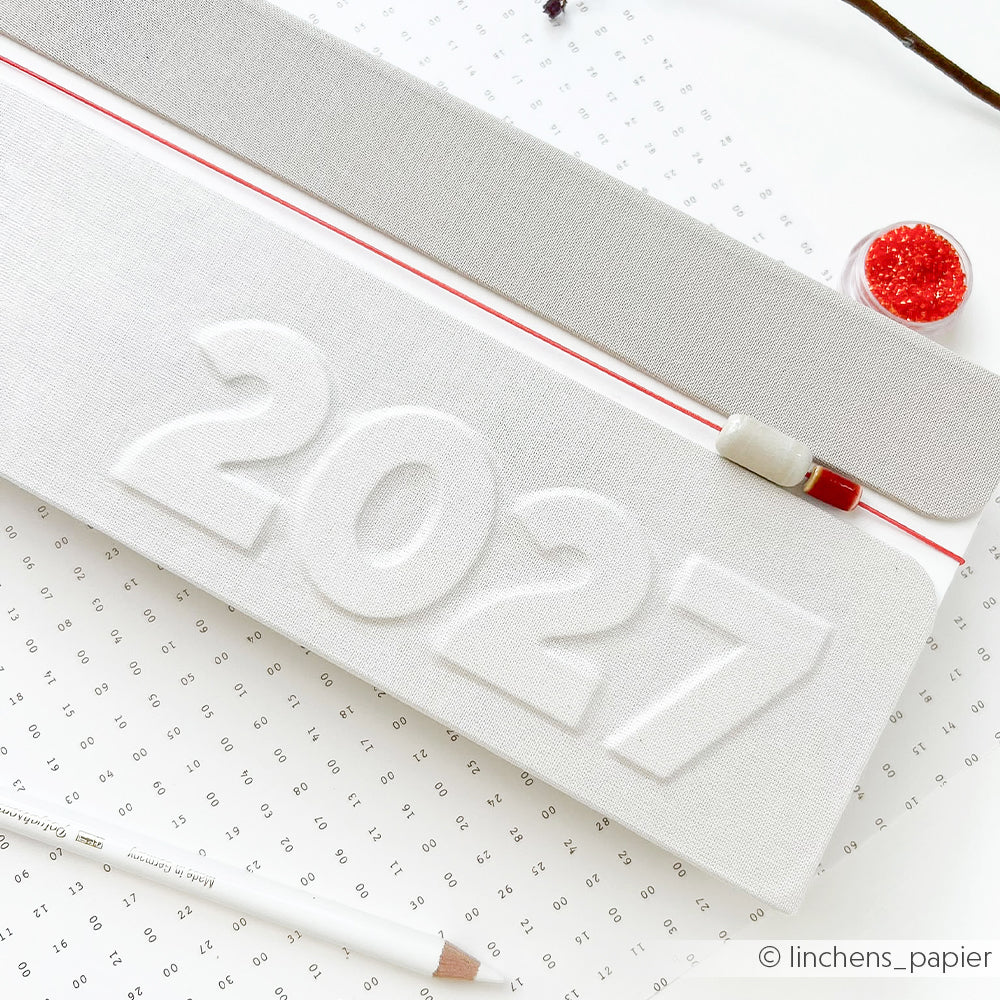 Weißer Planer für 2027 mit erhabenen Zahlen, rotem Reißverschluss, Bleistift und Perlen auf gemustertem Hintergrund – perfekt für alle, die sich von PAPPKit inspirieren lassen oder einen Kalender selbst gestalten möchten. Dieser stilvolle Kalender 2027 bringt Kreativität in Ihre tägliche Planung.