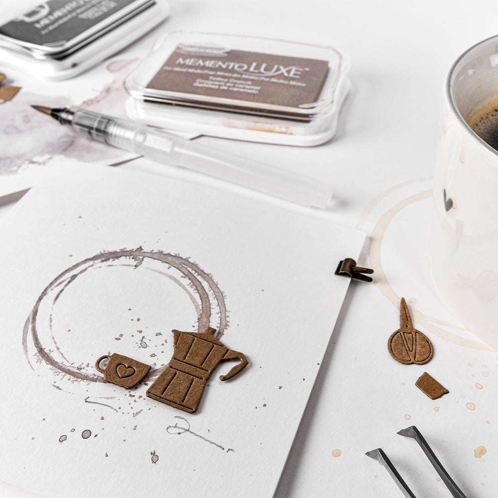 Eine handgefertigte Karte zum Thema Kaffee von Alexandra Renke, die mit Stempeln mit brauner Tinte unter Verwendung des Espresso-Sets und der DieCut Systeme hergestellt wurde, zeigt einen Stift und einen Kaffeebecher auf einem weißen Tisch.