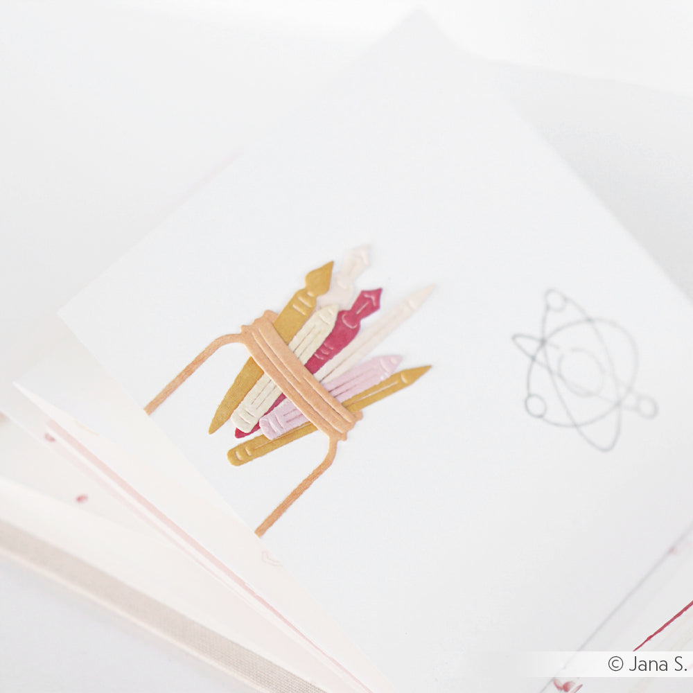Eine Zeichnung von fünf zusammengebundenen Buntstiften neben einem Atomsymbol auf einem weißen Blatt Papier – ideal, um Alexandra Renkes „Motivstanze Stifte & Pinsel“ in Szene zu setzen oder mit ihren kreativen „DieCut-Systemen“ und „Designpapieren“ zu experimentieren.