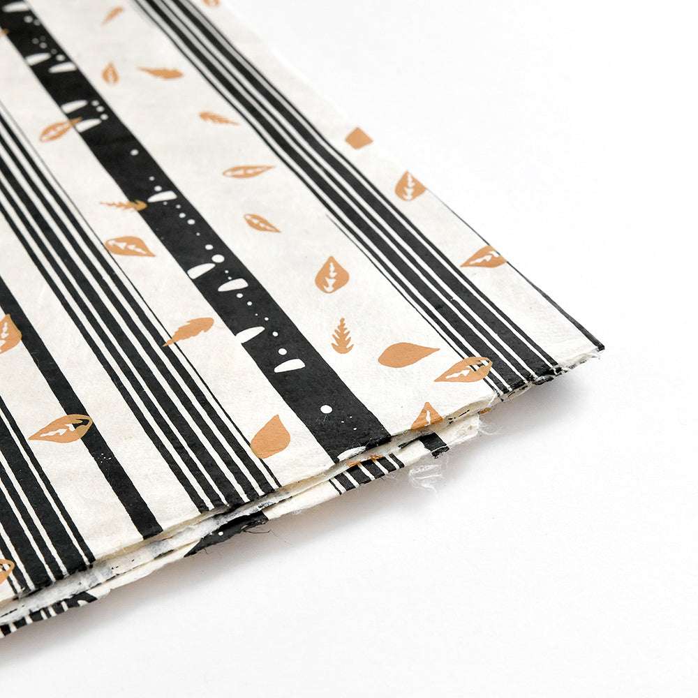 Stapel von ☆ gemusterten Nepalpapieren mit schwarzen Streifen und braunen Blättern auf weiß, ideal für Buchbinden oder Geschenke Verpacken, schräg gestellt.