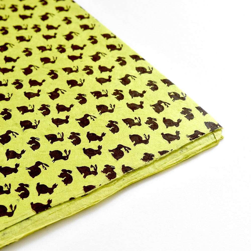 ☆ gelbe Nepalpapiere mit einem sich wiederholenden schwarzen Hasenmuster, schräg auf weißem Hintergrund - ideal zum Verpacken von Geschenken oder für Buchbindearbeiten.