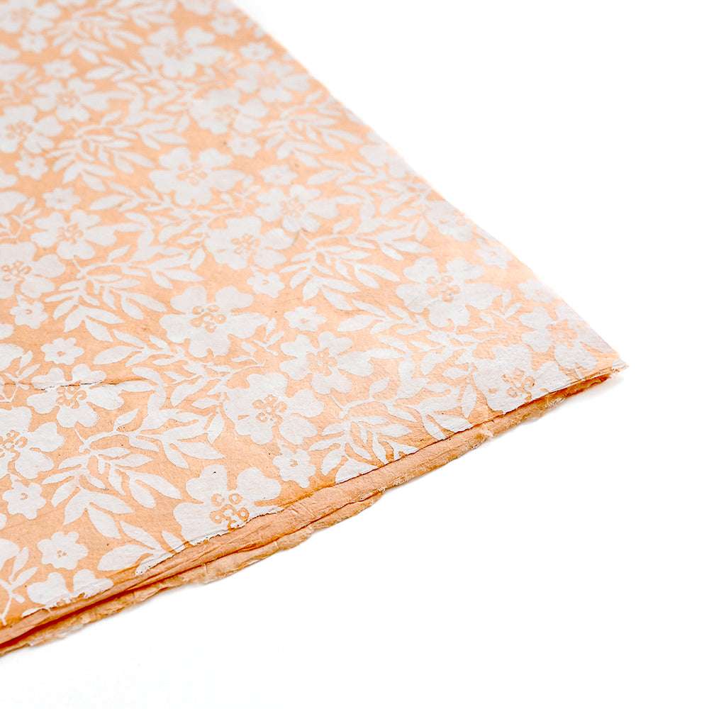 Pfirsichfarbene Nepalpapiere von ☆ mit weißem Blumenmuster, das von der Ecke aus auf weißem Hintergrund gezeigt wird - ideal zum Buchbinden oder Einwickeln liebevoller Geschenke.