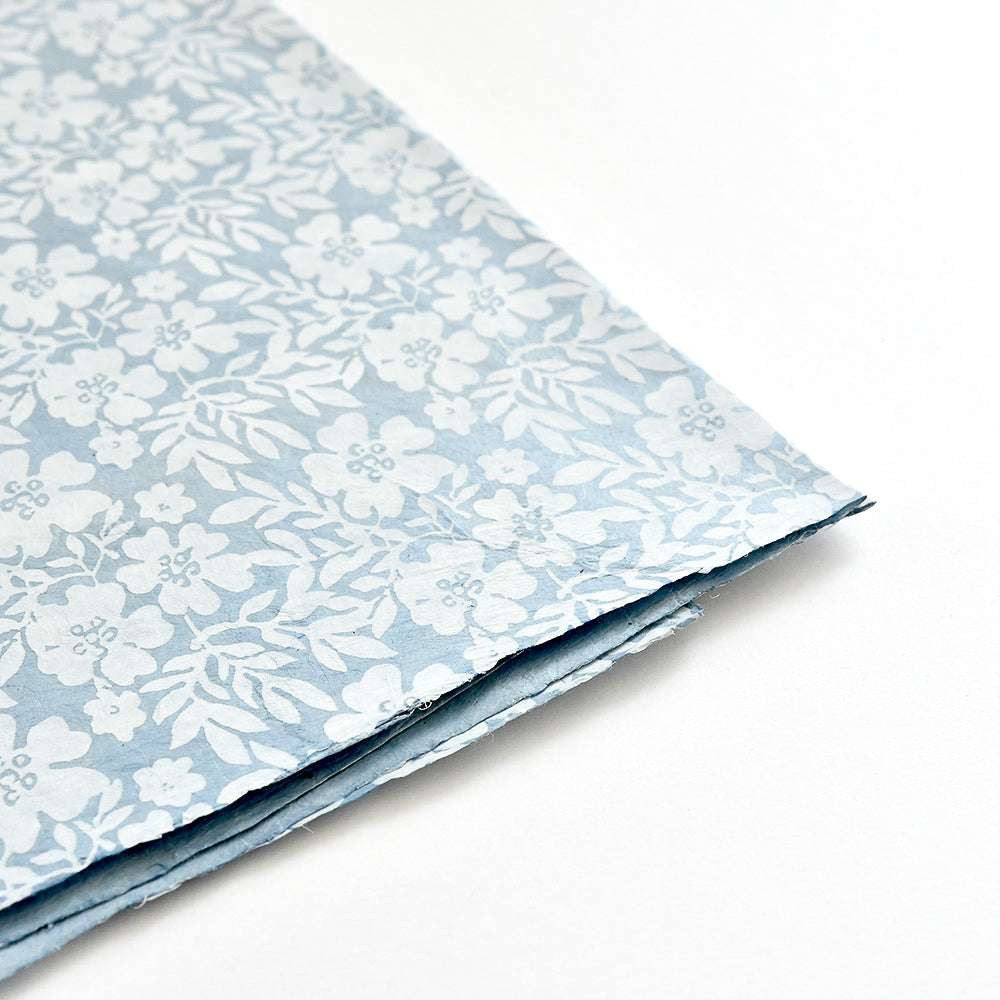 Ein Stapel blauer Nepalpapiere von ☆ mit einem weißen Blumenmuster - ideal für Buchbinden oder Geschenke Verpacken - auf weißem Hintergrund.