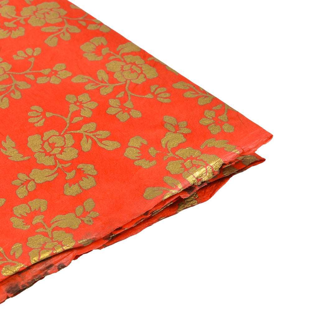 Orangefarbener Stoff mit goldenem Blumenmuster von ☆, sauber gefaltet auf weißem Grund - ideal für kreative Projekte oder Geschenkverpackungen, die das einzigartige Flair von Nepalpapier und Blütenmuster Rot widerspiegeln.