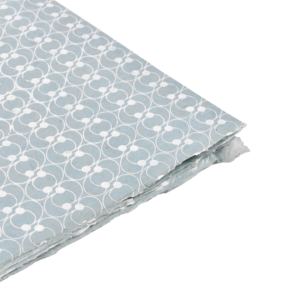 Ein Stapel blaues Nepalpapier von ☆ mit einem sich wiederholenden weißen geometrischen Muster, das in einer Ecke gezeigt wird - ideal zum Buchbinden oder stilvollen Verpacken von Geschenken.
