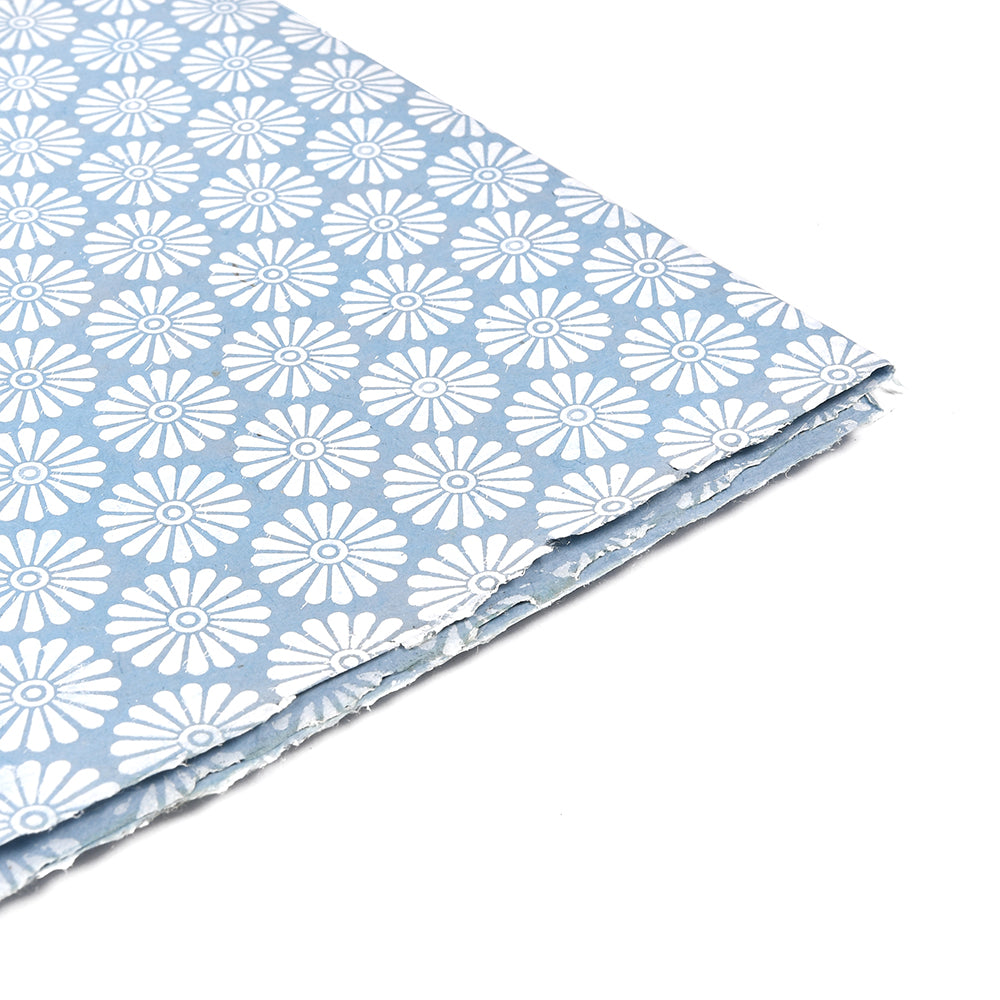 Gefaltetes blaues Nepalpapier mit weißen Gänseblümchen in ordentlichen Reihen auf weißem Hintergrund - ein wunderschönes, nachhaltiges Papier, das sich ideal zum Verpacken besonderer Geschenke eignet.