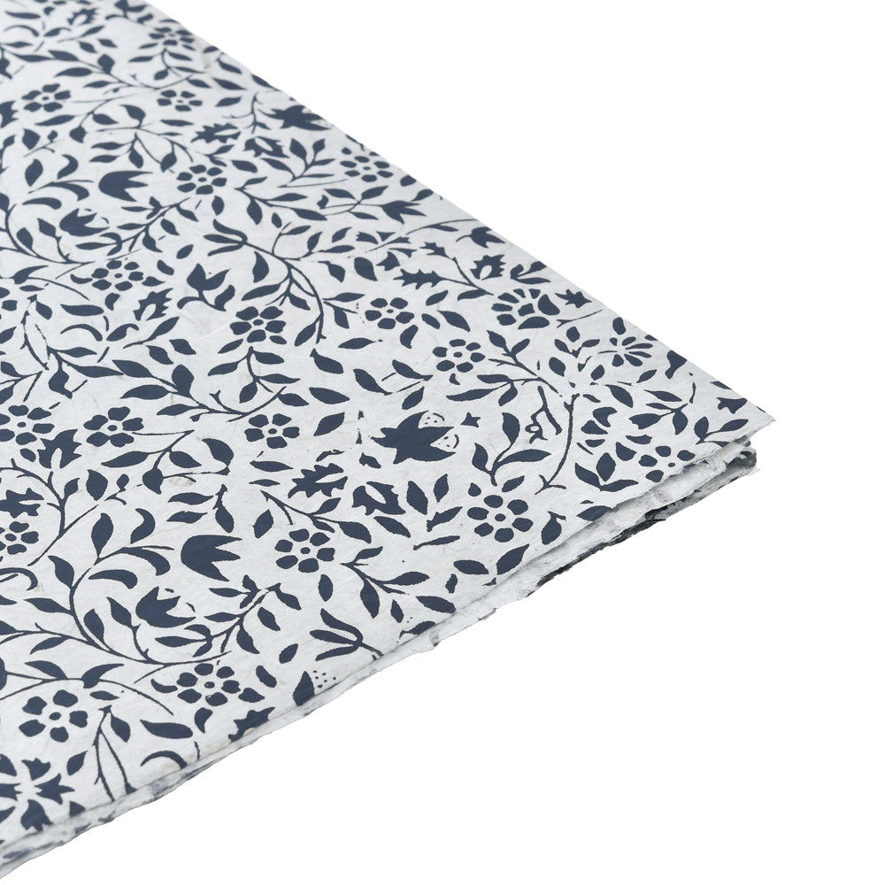 Ein Blatt ☆ Nepalpapier in weiß mit marineblauem Blumen- und Blattmuster, an der Ecke teilweise gefaltet - perfekt als nachhaltiges Papier für besondere Geschenkverpackungen.