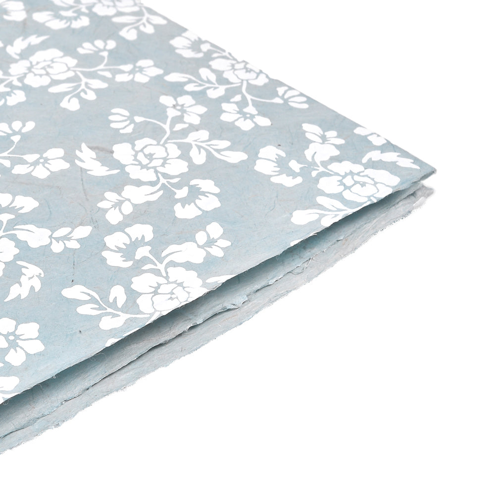 Handgefertigtes hellblaues Nepalpapier mit weißem Blumenmuster von ☆, schräg auf weißem Hintergrund - ideal für Geschenkverpackungen.