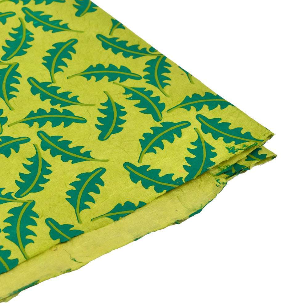 Gelb-grünes Nepalpapier von ☆ mit grünen Blattmustern und einer gefalteten Ecke auf Weiß - perfekt zum Buchbinden oder Verpacken von Geschenken.