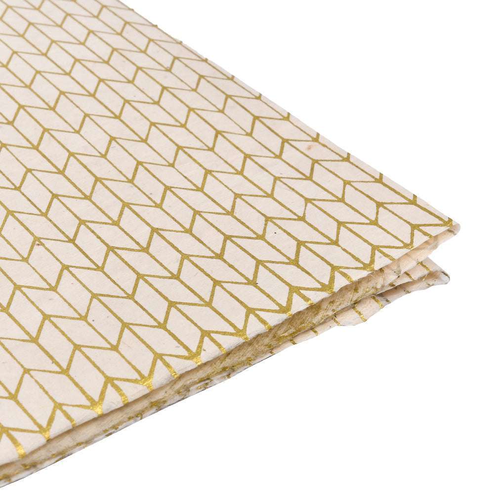 Der gefaltete ☆ Stoff zeigt ein goldenes geometrisches Würfelmuster auf hellem Creme, ideal für Geschenke Verpacken. Ausgestellt auf einer weißen Oberfläche.
