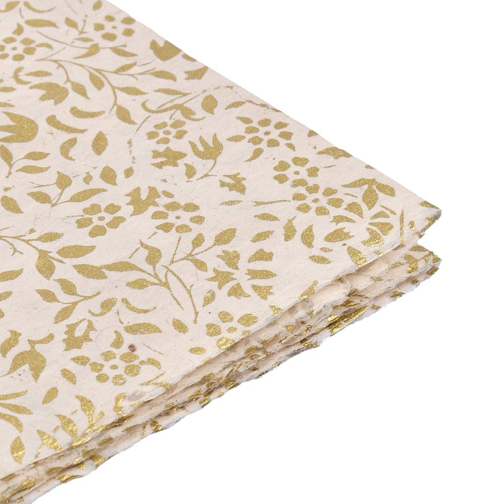 Cremefarbenes handgeschöpftes Nepalpapier mit goldenem Blumenmuster, an den Ecken gestapelt - ideal zum Buchbinden oder Verpacken von Geschenken, auf weißem Hintergrund.