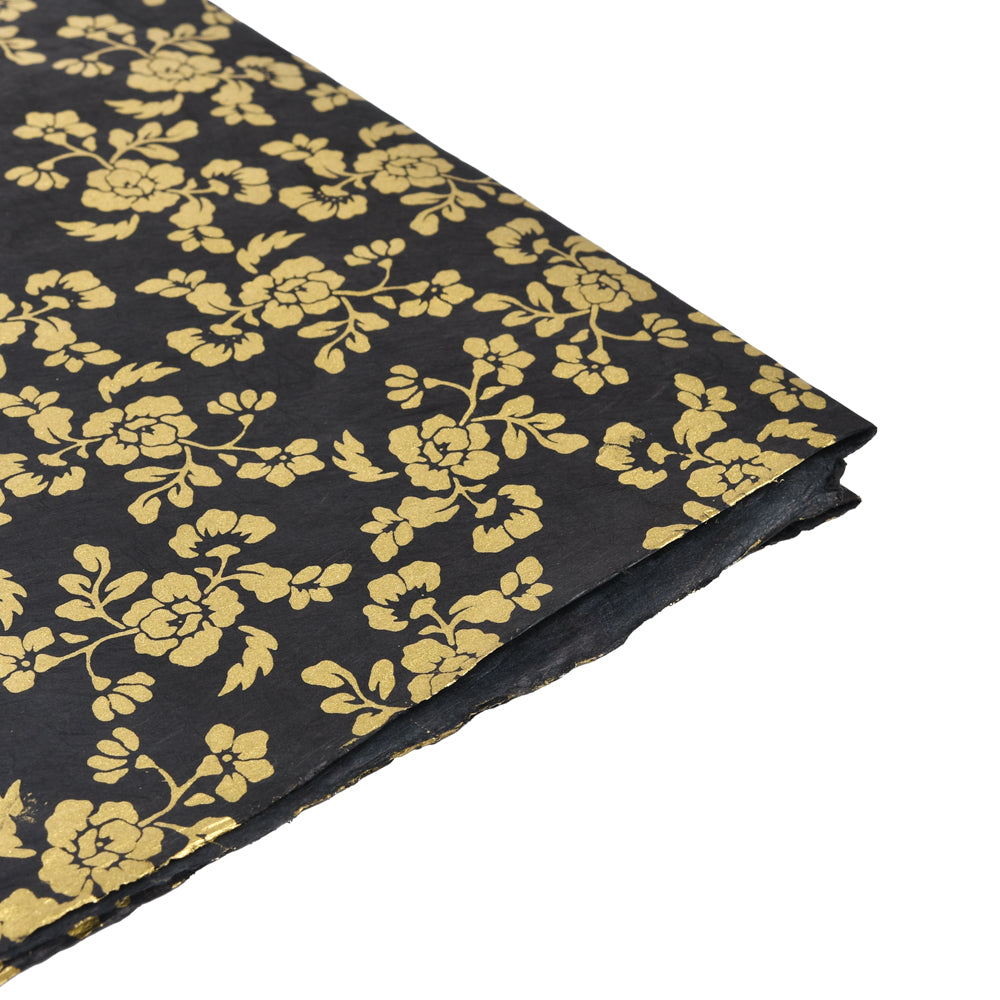 ☆ Schwarzes Nepalpapier mit einem goldenen Blütenmuster Schwarz in Nahaufnahme auf gestapelten Blättern - ideal als nachhaltiges Geschenkpapier.