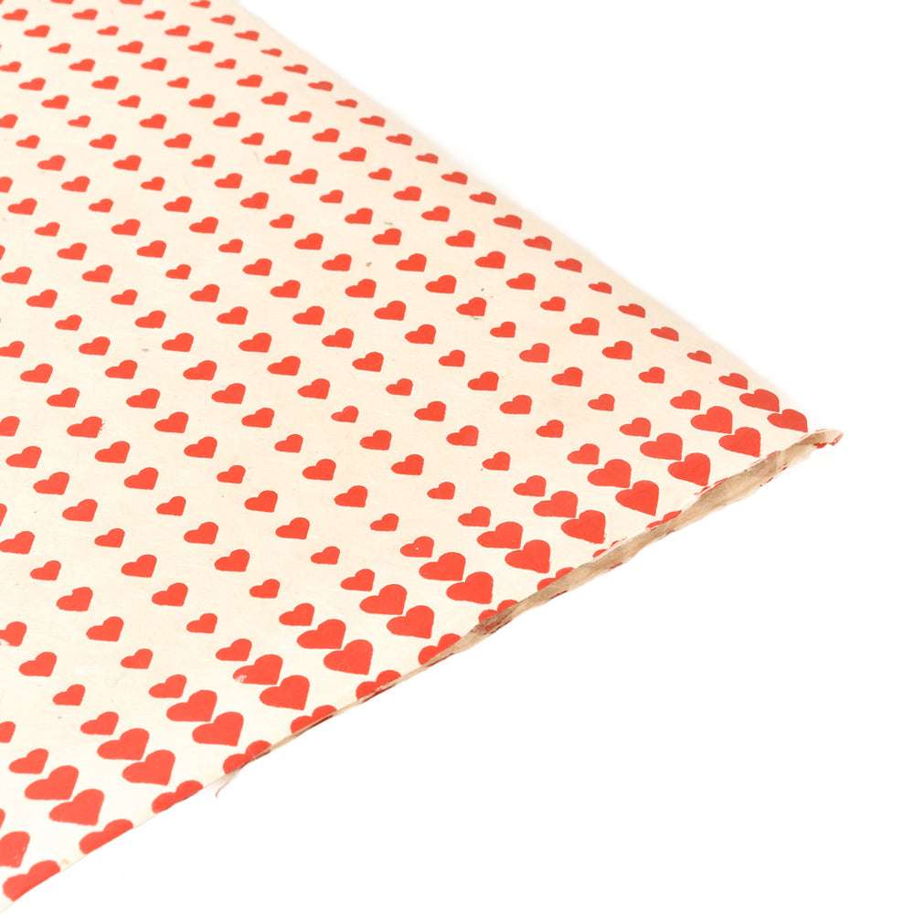 Ein Blatt ☆ Nepalpapier mit einem sich wiederholenden Muster aus kleinen roten Herzen auf cremefarbenem Grund - ideal zum Verpacken von Geschenken oder für Buchbindearbeiten.