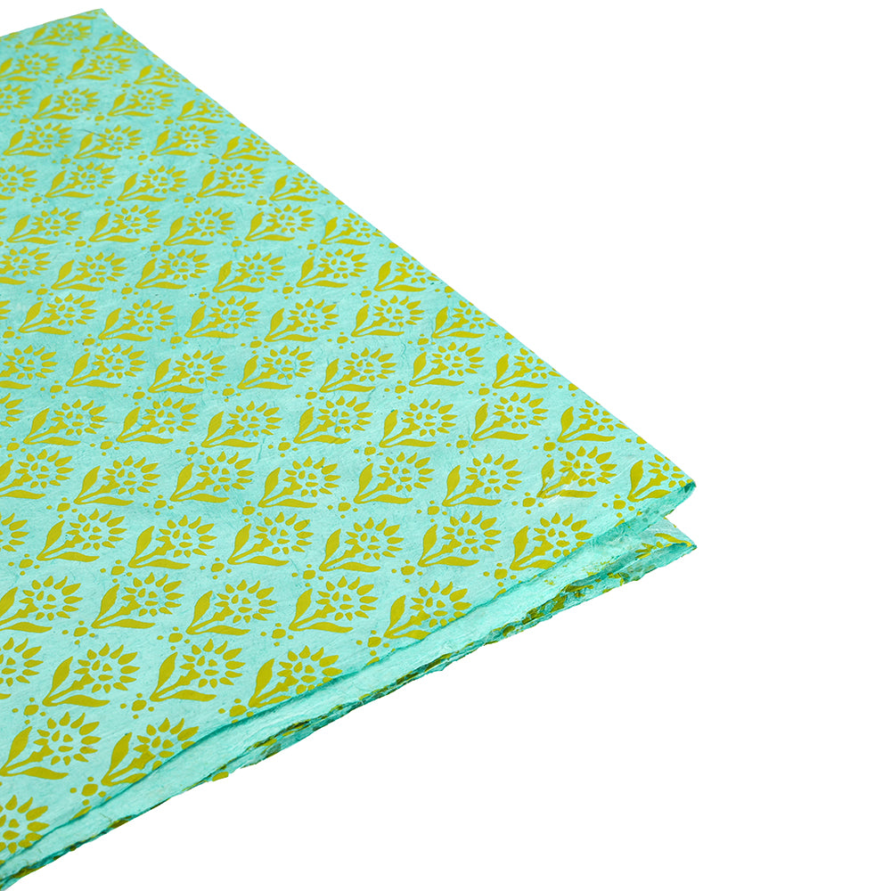 Gefalteter türkisfarbener Stoff mit gelbem Blumenmuster auf weißem Hintergrund von ☆, ideal für Geschenkverpackungen oder zum Kombinieren mit nachhaltigen Papierakzenten.
