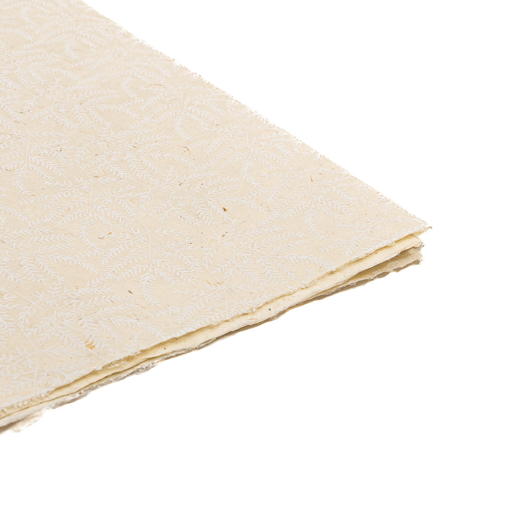 Ein Stapel cremefarbenes Nepalpapier von ☆ mit einem zarten Blattmuster – ideal für nachhaltiges Papier oder zum Verpacken von Geschenken mit einzigartigem, handwerklichem Flair.