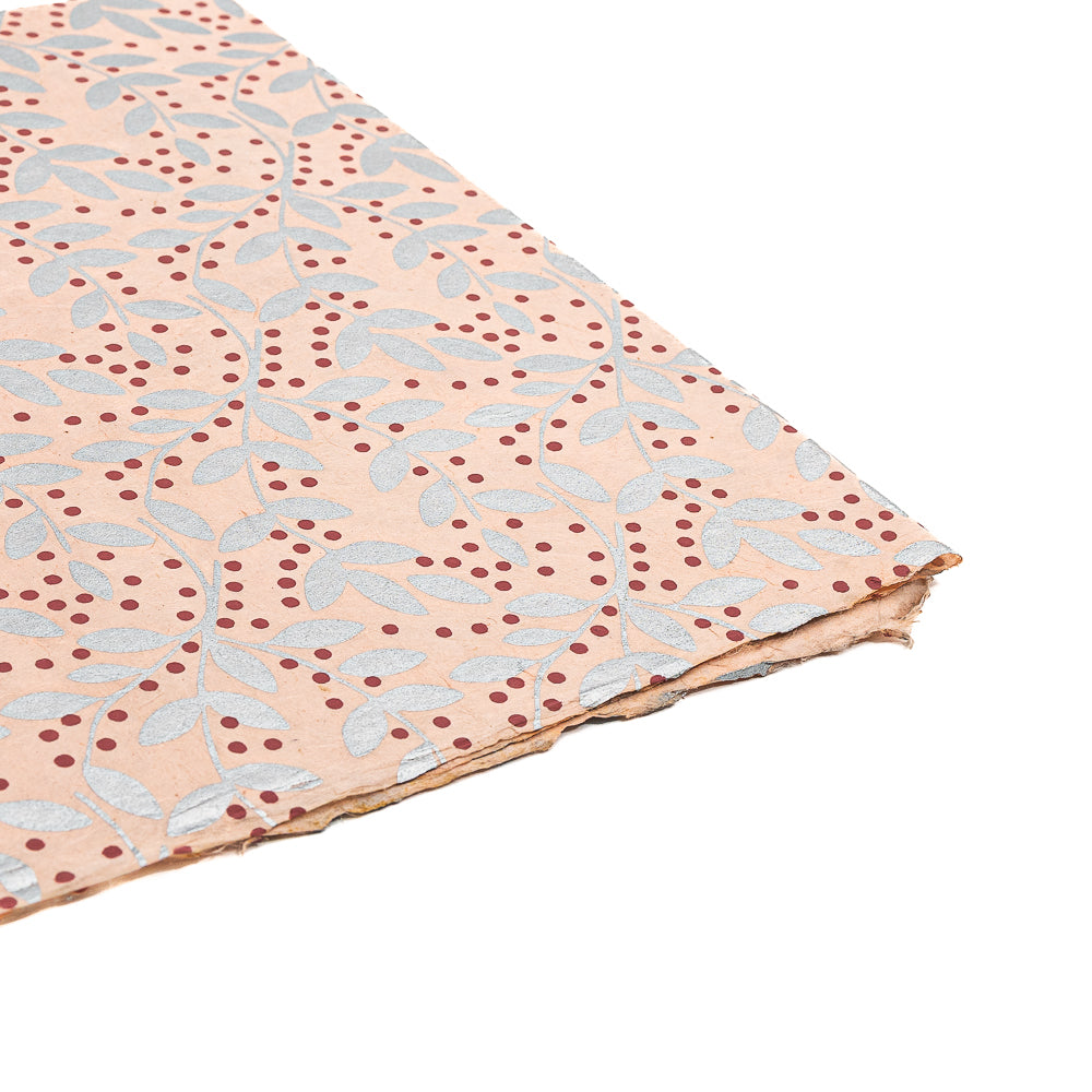 Ein Blatt nachhaltiges Papier von ☆ mit einem Blatt- und Punktmuster auf pfirsichfarbenem Hintergrund und leicht ausgefransten Rändern – ideal für Geschenkverpackungen oder Bastelarbeiten.