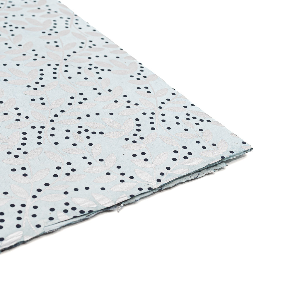 Hellblaues Nepalpapier von ☆ mit weißen Blättern und vereinzelten schwarzen Punkten, teilweise auf weißem Hintergrund abgebildet – ideal als umweltfreundliches Geschenkpapier oder handgeschöpftes Papier für besondere Anlässe.