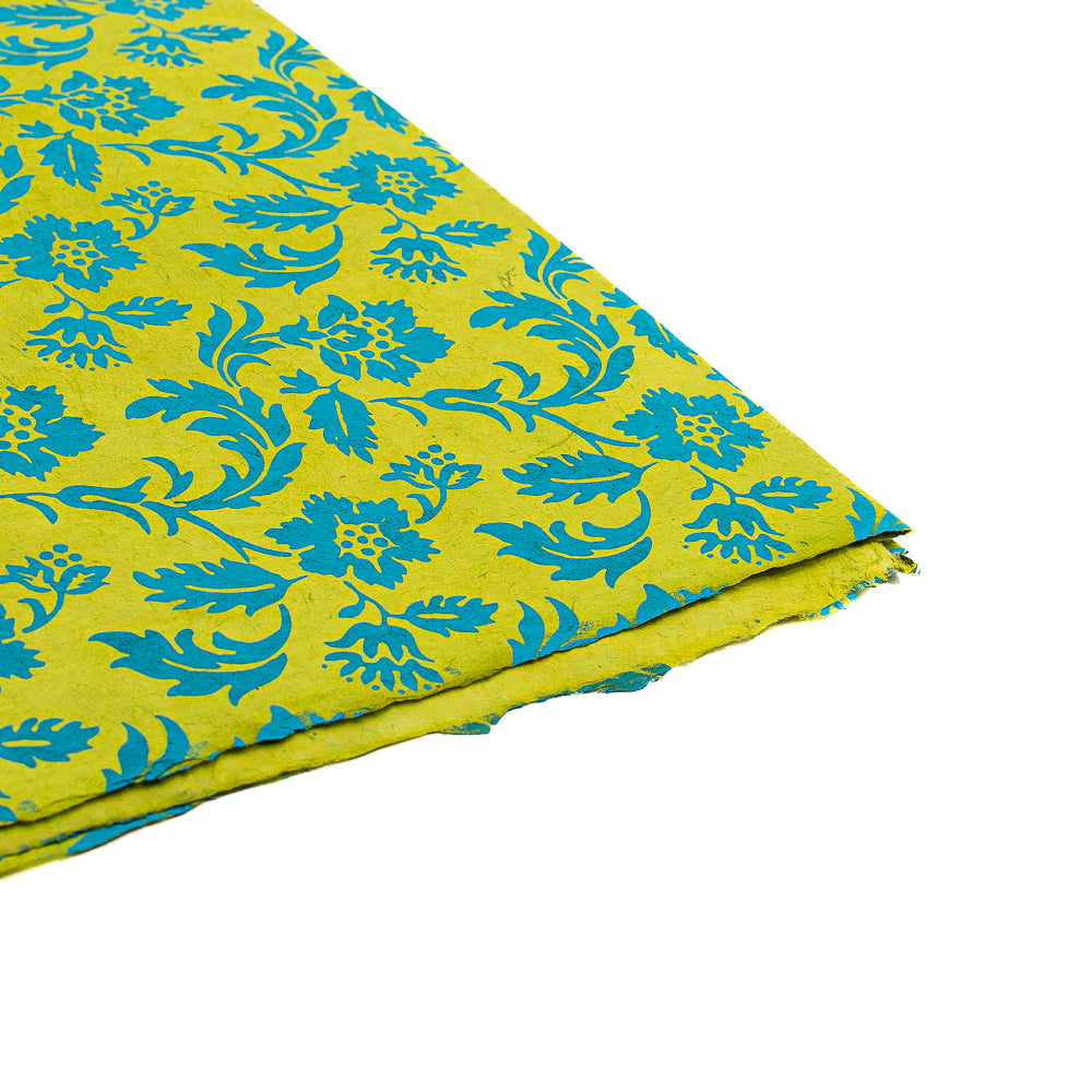 ☆ Gelber Stoff mit blauem Blumenmuster, an der Ecke gefaltet und auf weißem Untergrund liegend, erinnert an handgeschöpftes Papier – ideal für nachhaltige, einzigartige Geschenkverpackungen.